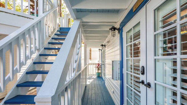 A covered wooden deck with blue steps and white railings, leading to a building with large windows and a door with a keypad lock. - Custom House Inn (Key West)