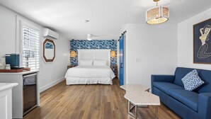 A bedroom with a bed, a blue sofa, a small table, a ceiling fan, and a wall-mounted air conditioner. - Custom House Inn (Key West)