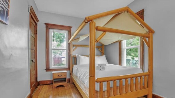 Ein Himmelsbett mit Baldachin, ein Nachttisch aus Holz und ein Fenster mit Jalousien.
