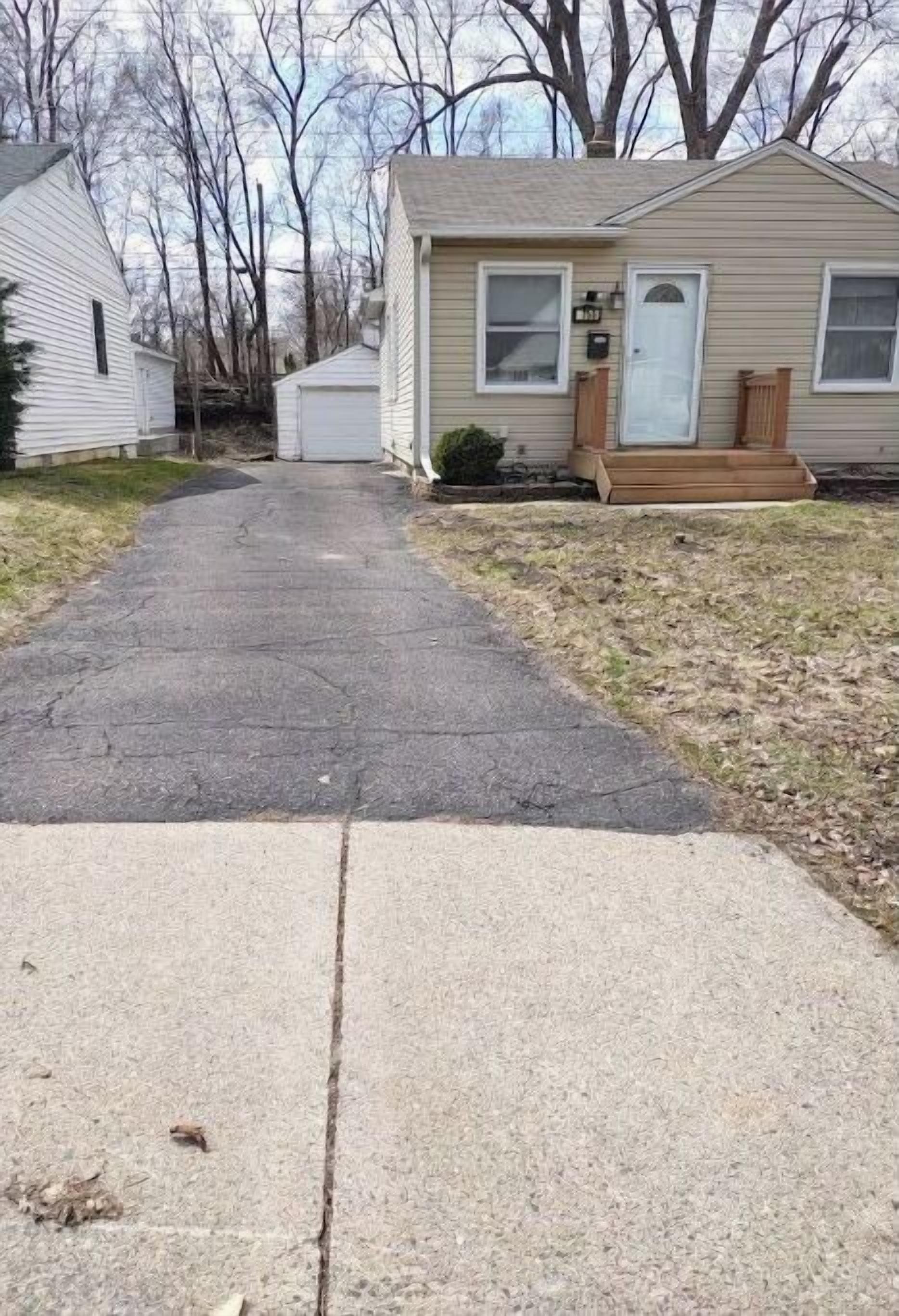 A residential driveway leading to a single-story house with a front porch and a mailbox.