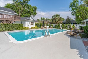 Ein Swimmingpool mit Holzdeck und Liegestühlen, umgeben von Häusern und Grünflächen.