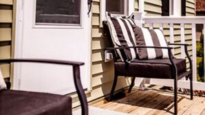 A porch with a wooden deck, a chair with a striped cushion, and a white door with a window. - Hollow Hideaway is just the place if you looking to get away and relax.   (Smithsburg)