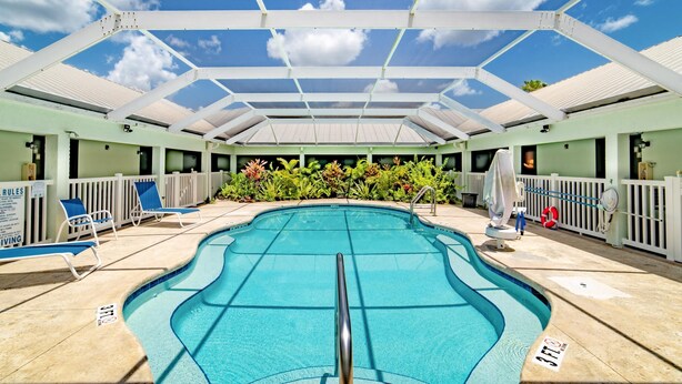 Piscina interior com água azul cristalina, rodeada por espreguiçadeiras e uma área coberta com telhado branco.