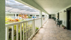Uma área externa coberta com cerca branca, plantas em vasos e chão de azulejos.