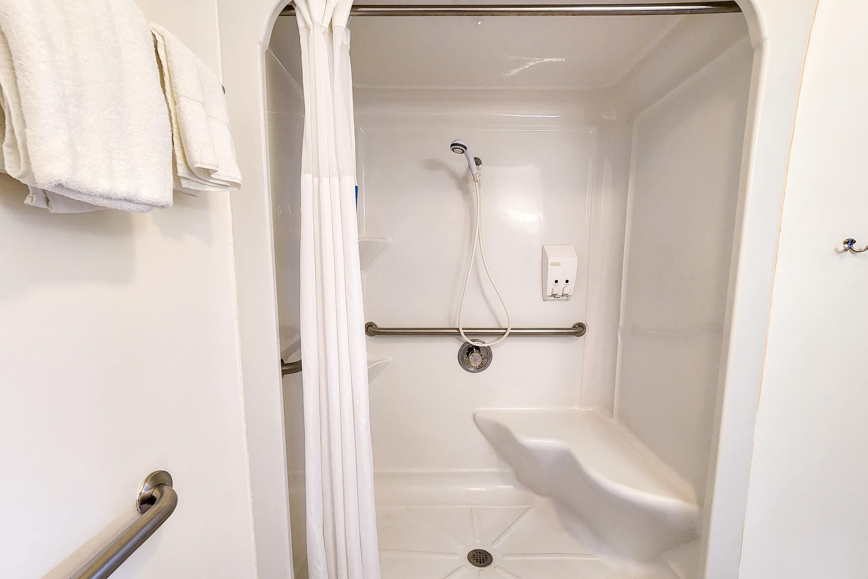 A white, enclosed shower area with a handheld showerhead, a grab bar, and a white toilet.