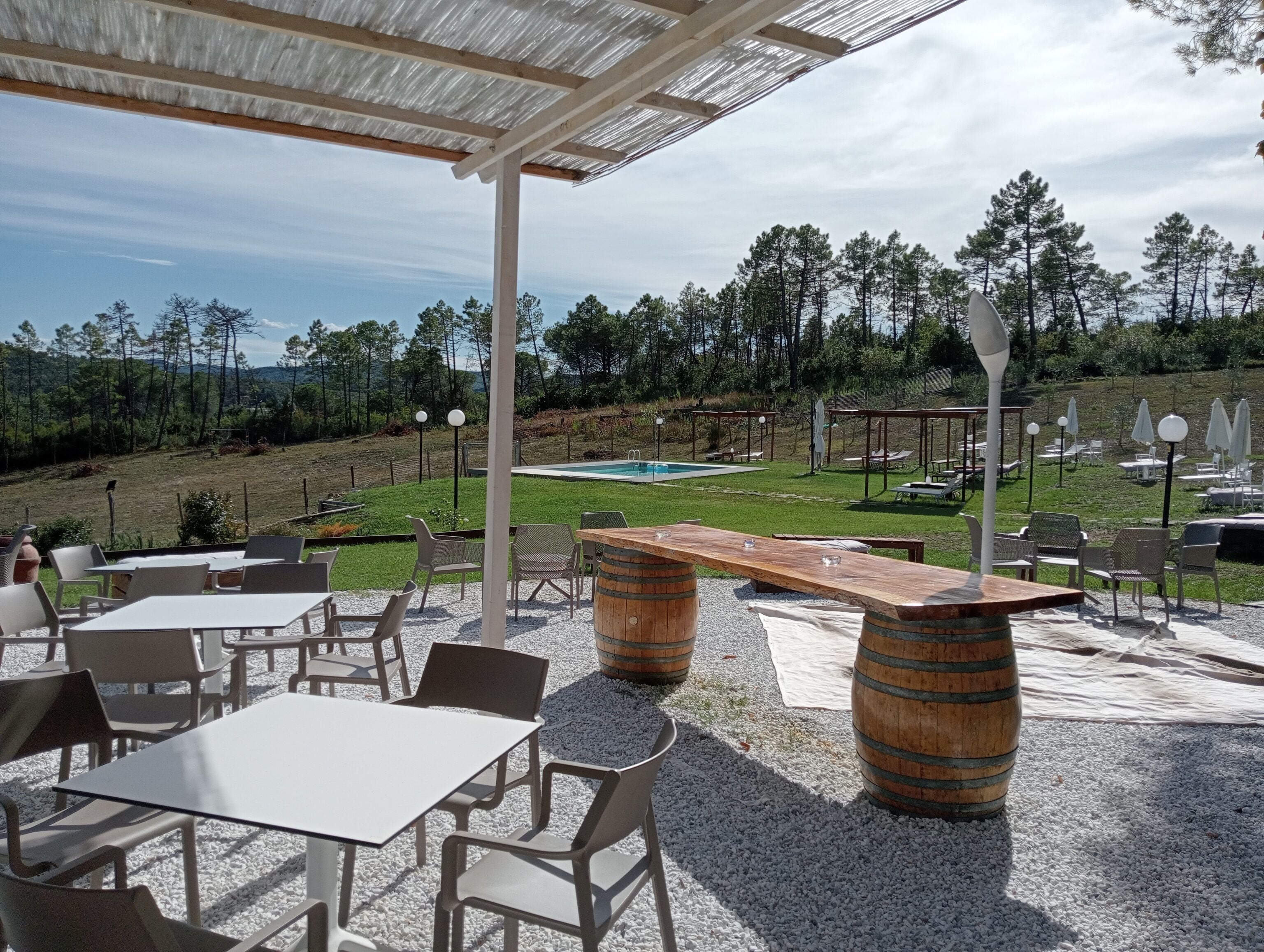 An outdoor patio with tables and chairs, a wooden barrel, and a pool in the background.