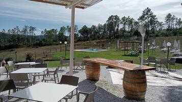 An outdoor patio with tables and chairs, a wooden barrel, and a pool in the background.