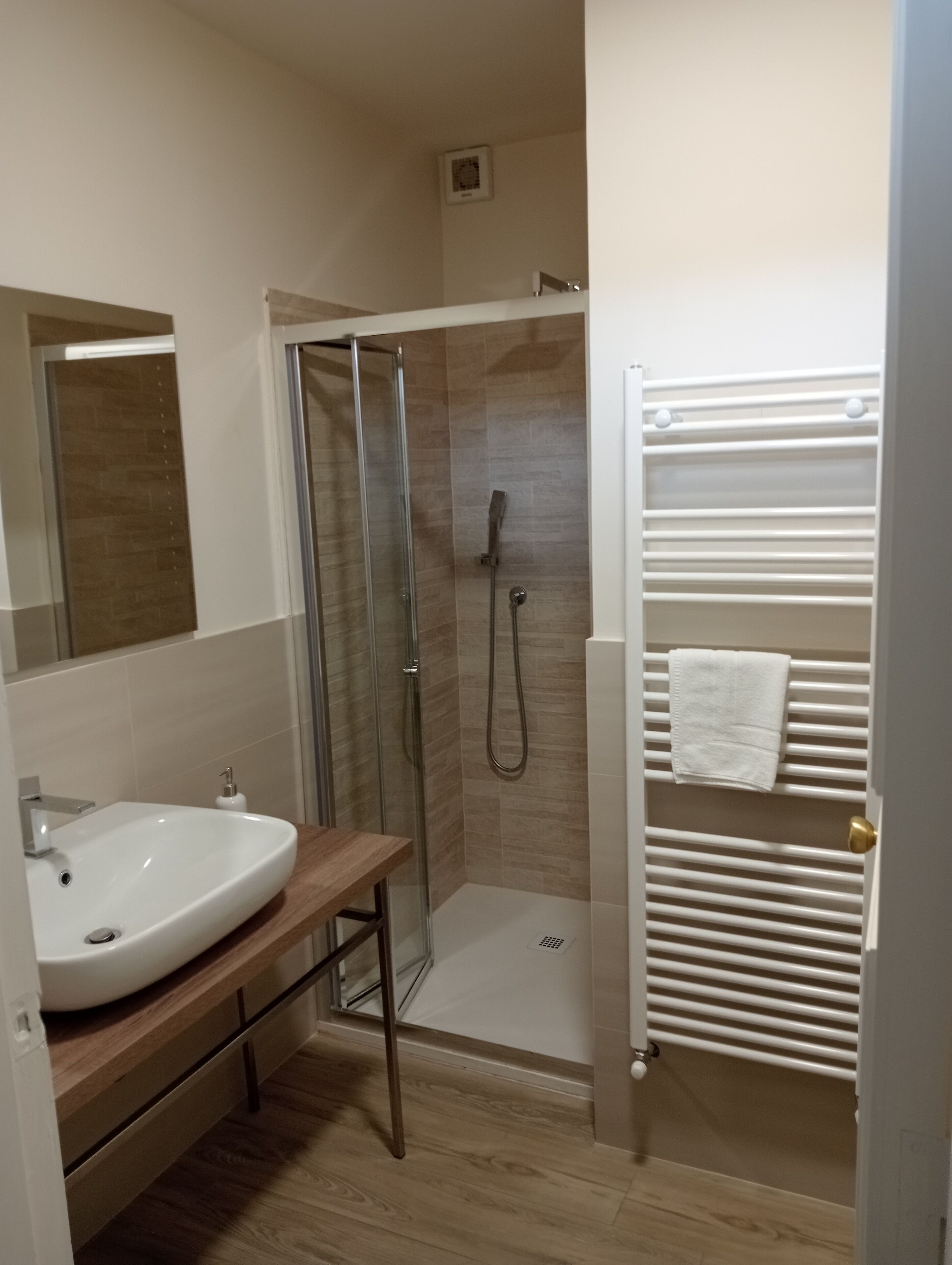 Ein modernes Badezimmer mit einer Duschkabine, einem Holzausziehtisch mit Waschbecken und einem weißen Handtuchhalter.