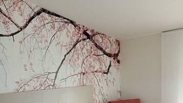 A bedroom with a bed, a nightstand, a red chair, and a wall with a cherry blossom tree mural.