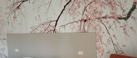 A bedroom with a bed, a nightstand, a red sofa, and a wall with a cherry blossom mural.