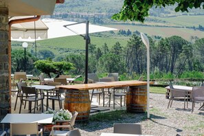 An outdoor seating area with tables and chairs, a wooden bar, and a view of the countryside. - Casa di Palaia (Greve in Chianti)