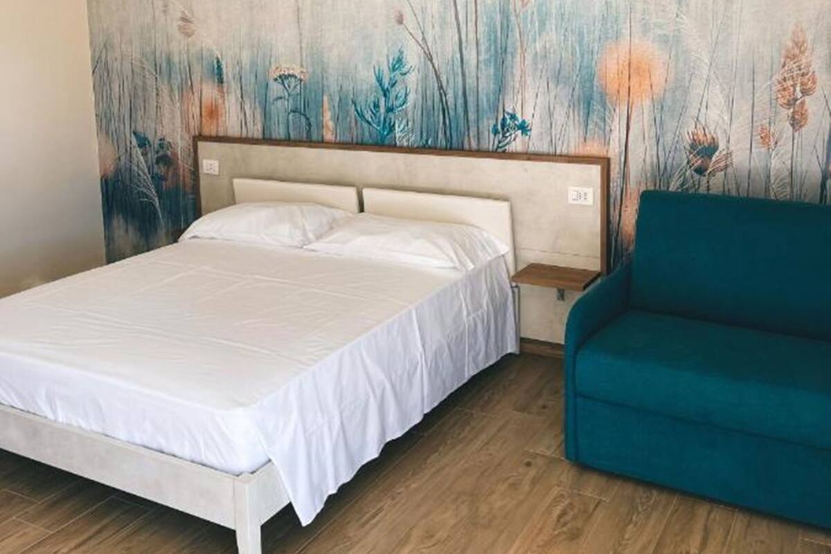 A bedroom with a bed, a teal armchair, and a wall mural.
