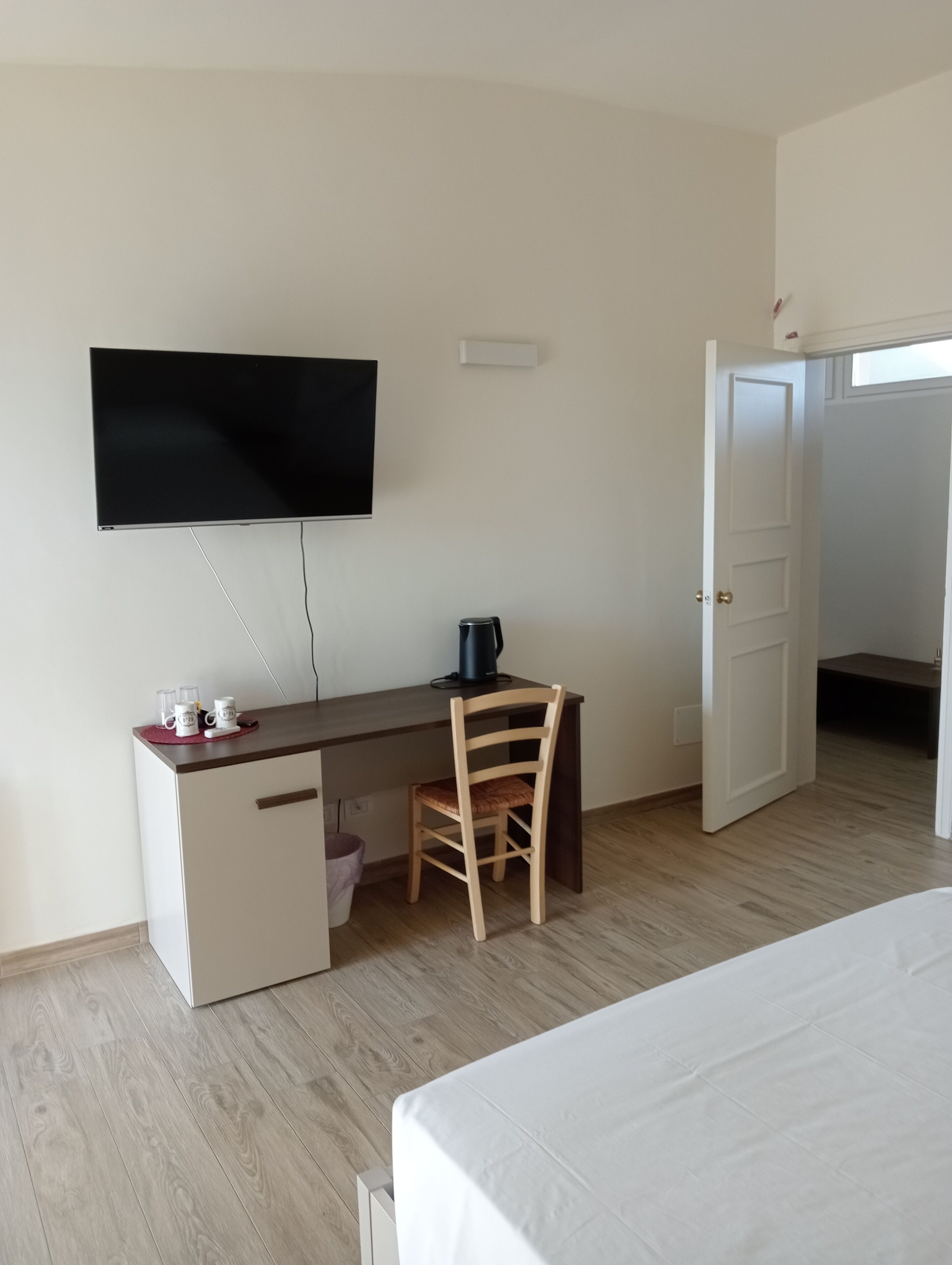 Un dormitorio con cama, un escritorio con silla, televisión y una puerta.