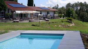 A swimming pool with a wooden deck, a covered outdoor seating area, and a house with a red roof in the background. - Casa di Palaia (Greve in Chianti)