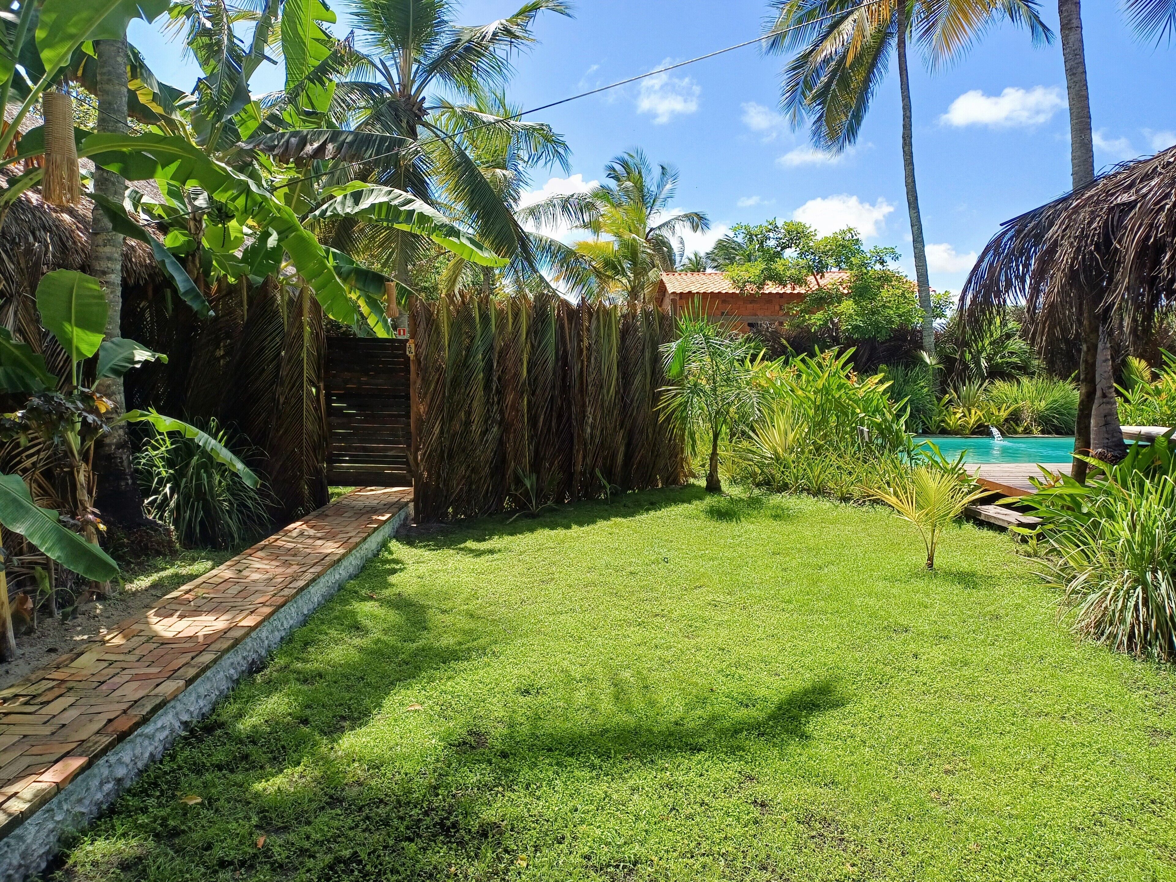 A well-maintained garden with a brick pathway leading to a pool area surrounded by lush greenery and palm trees.