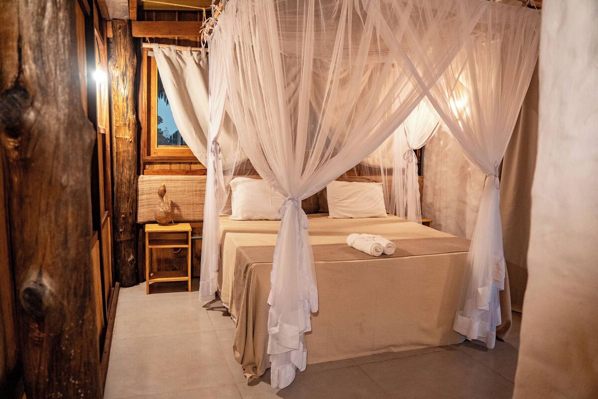 Quarto com cama de dossel, paredes de madeira e uma pequena mesa com abajur.