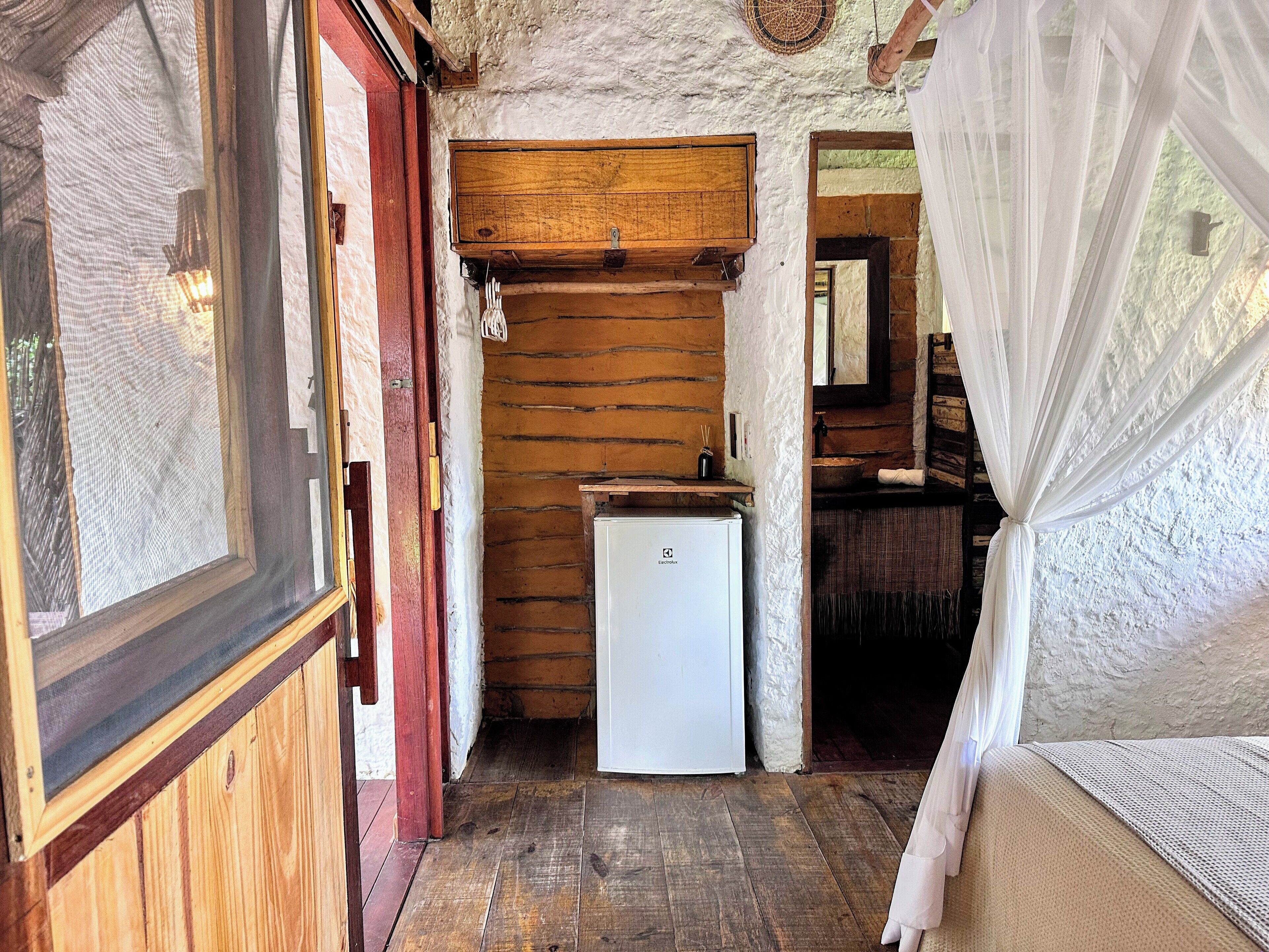 Een rustiek houten interieur met een houten plafond, een kleine witte koelkast en een houten kast.