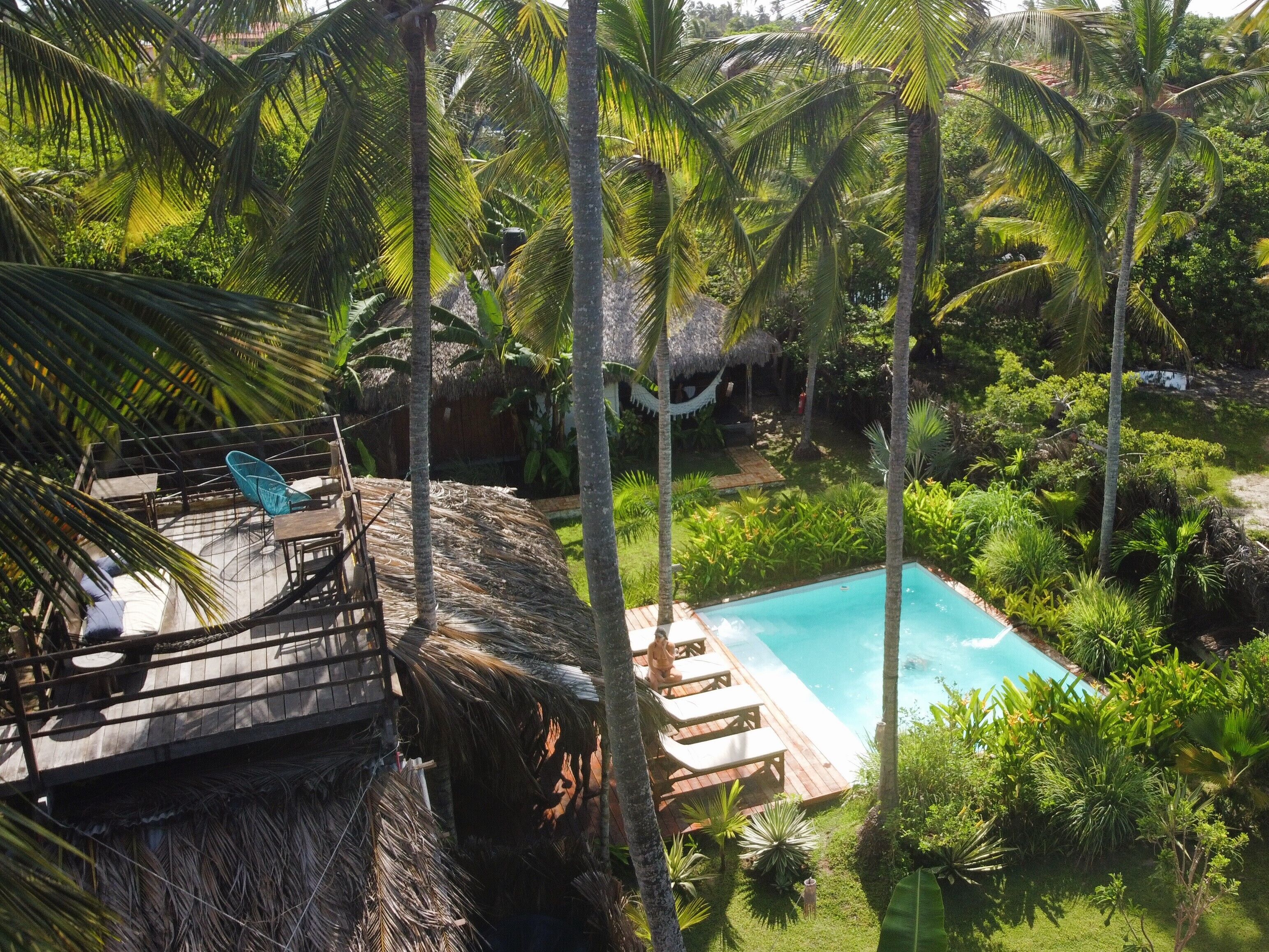 A tropical resort with a pool, wooden deck, and thatched-roof structures.