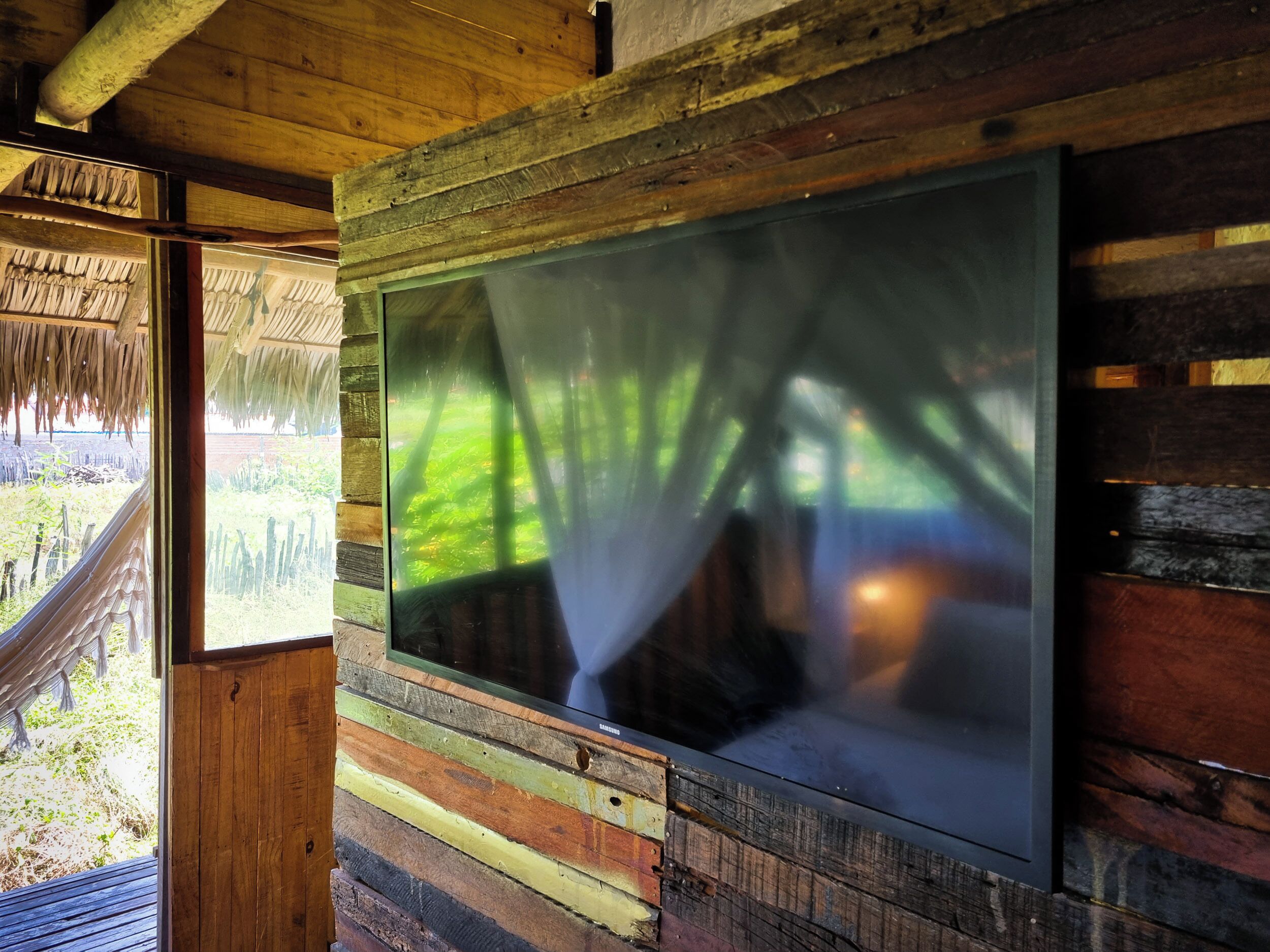 A room with a large window, wooden walls, and a thatched roof visible through the window.