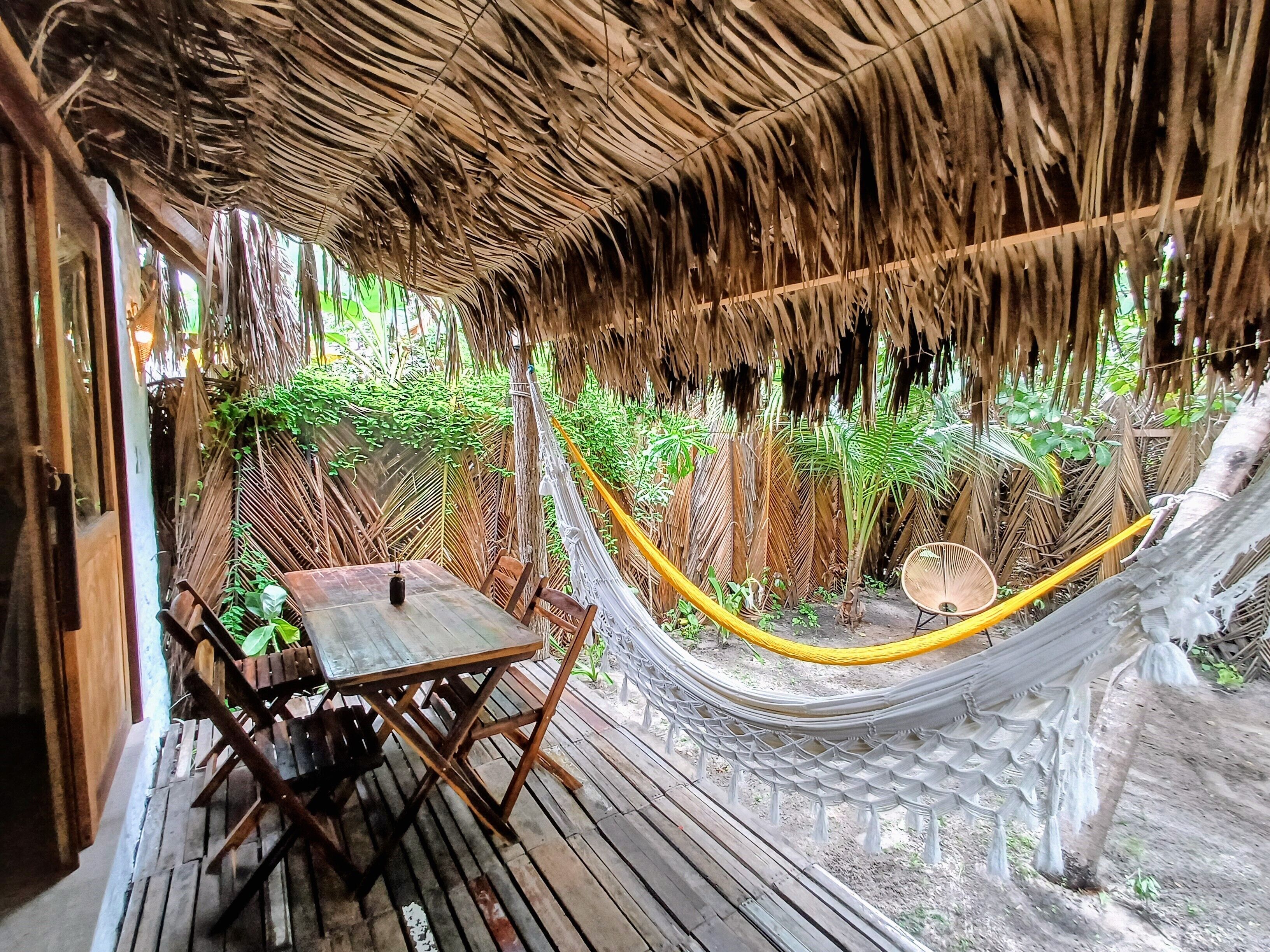 A hammock under a thatched roof, wooden furniture, and lush greenery.
