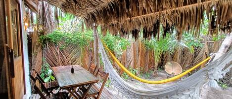 A hammock under a thatched roof, wooden furniture, and lush greenery.