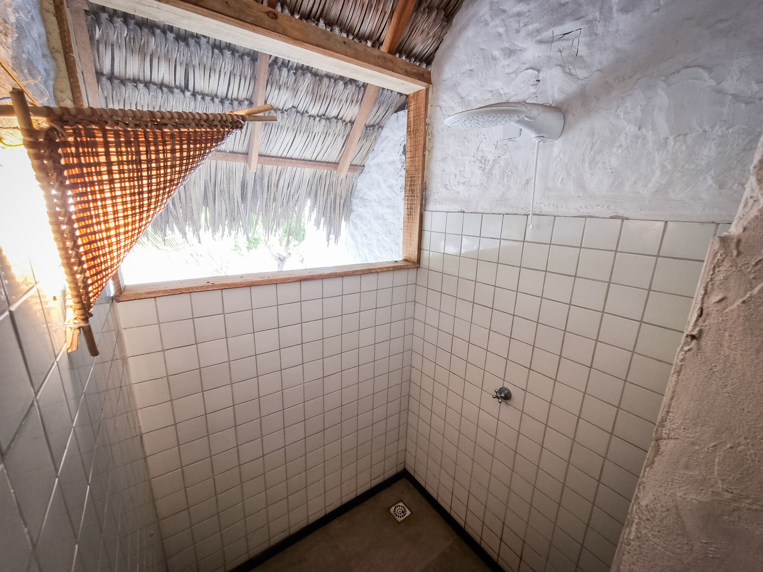 A small, tiled bathroom with a window and a showerhead.