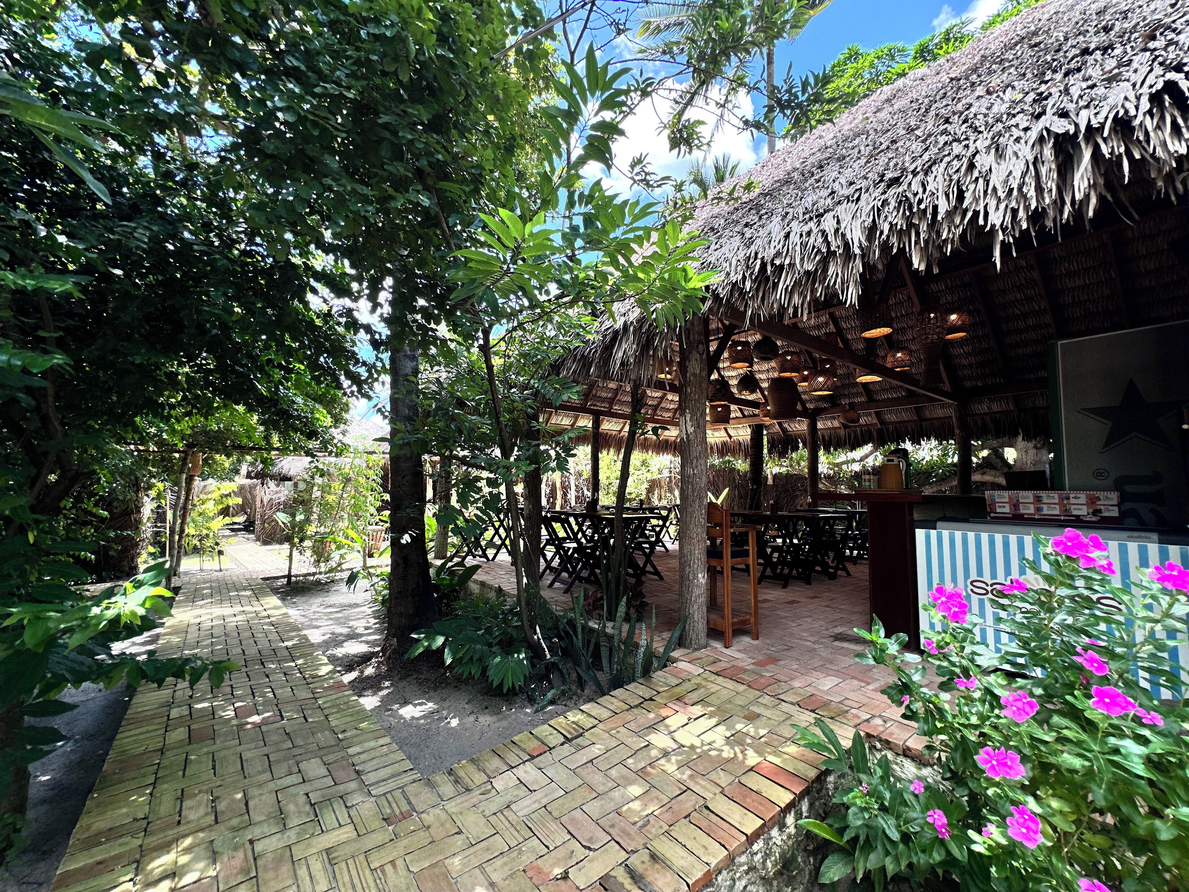 A thatched-roof outdoor seating area with brick pathways and lush greenery.