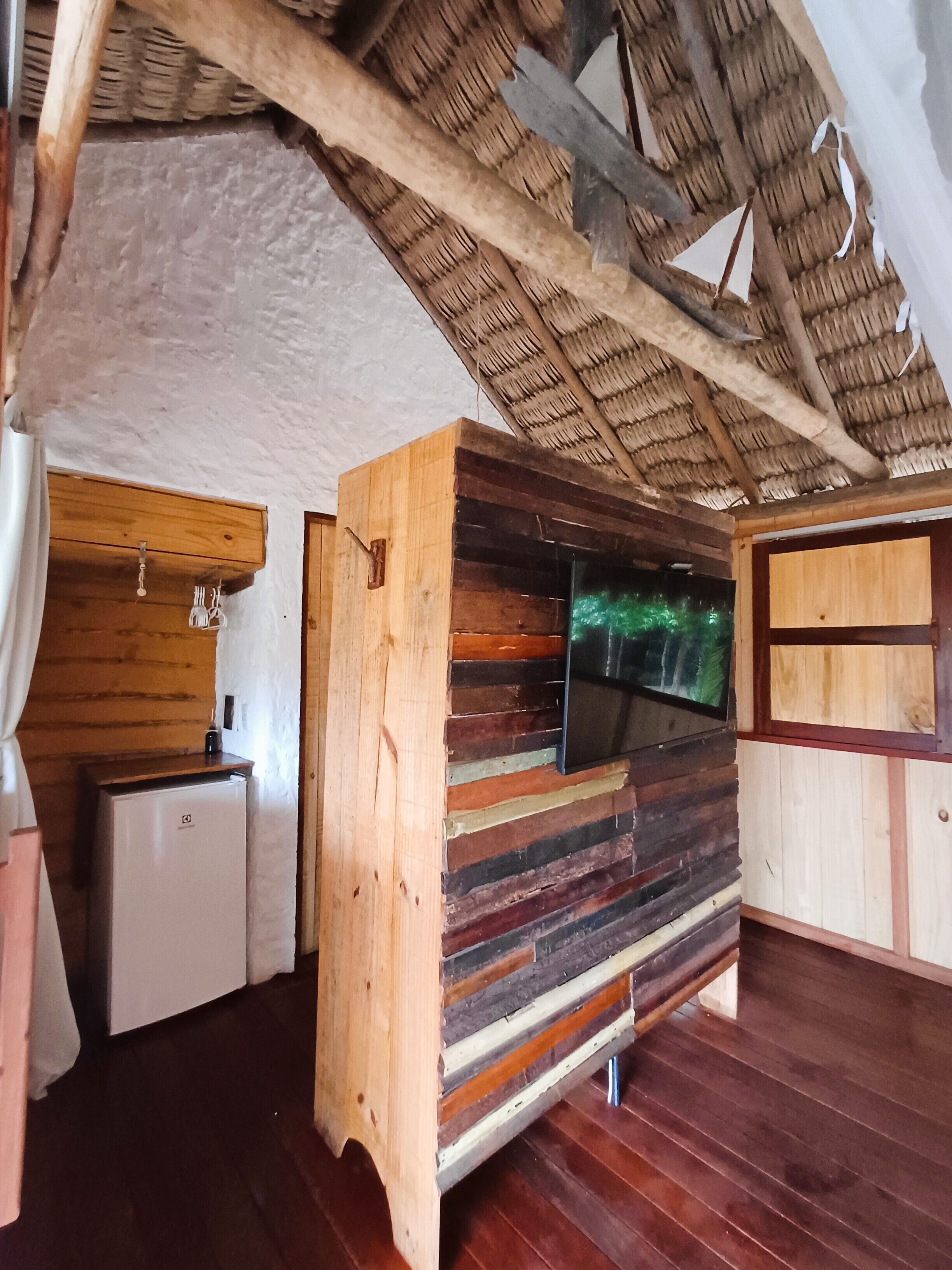 Ein rustikales Blockhaus-Interieur mit einer hölzernen Bank, einem kleinen Kühlschrank und einem an der Wand befestigten Fernseher.