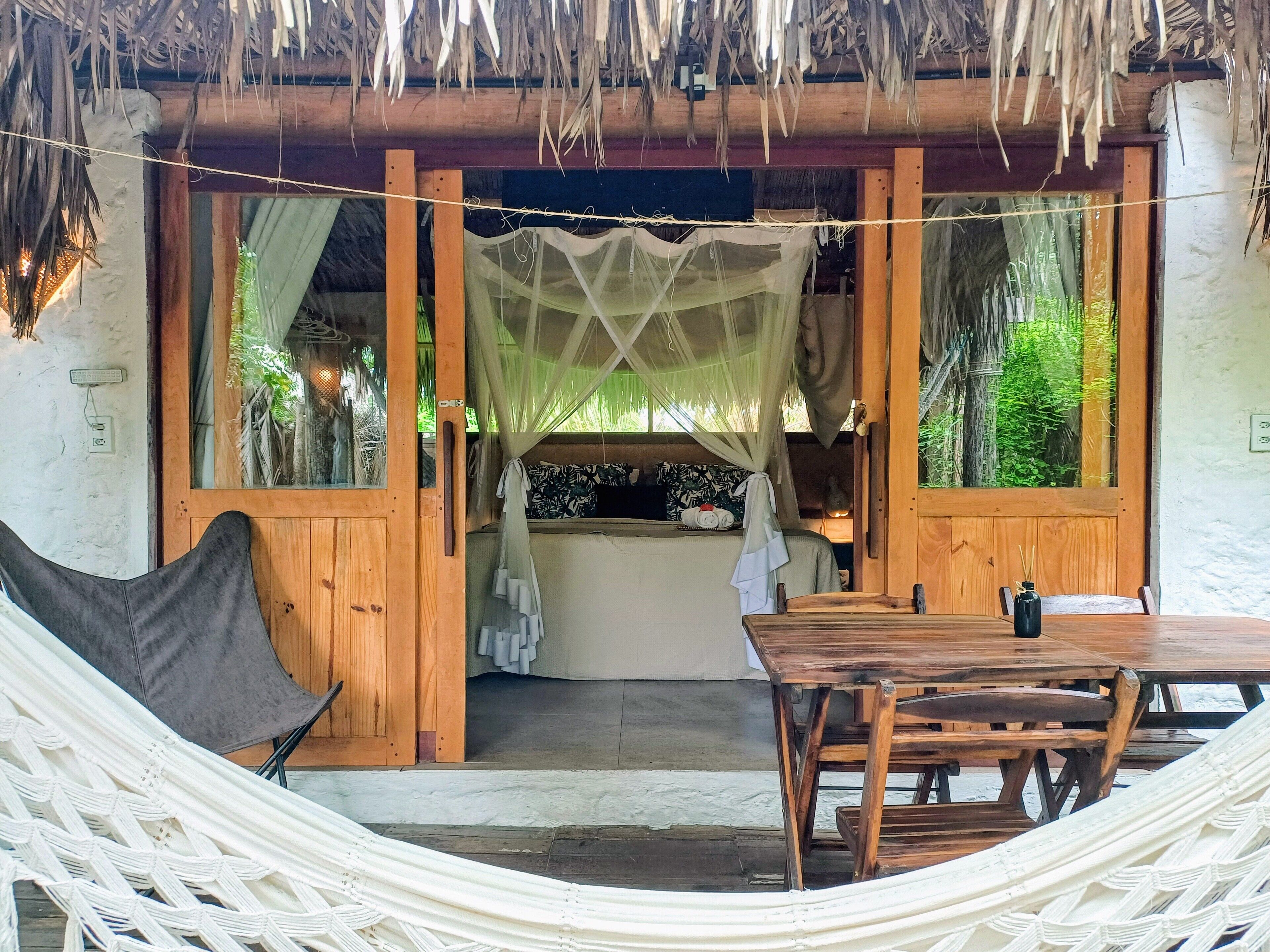 A cozy room with a hammock, wooden furniture, and a thatched roof.