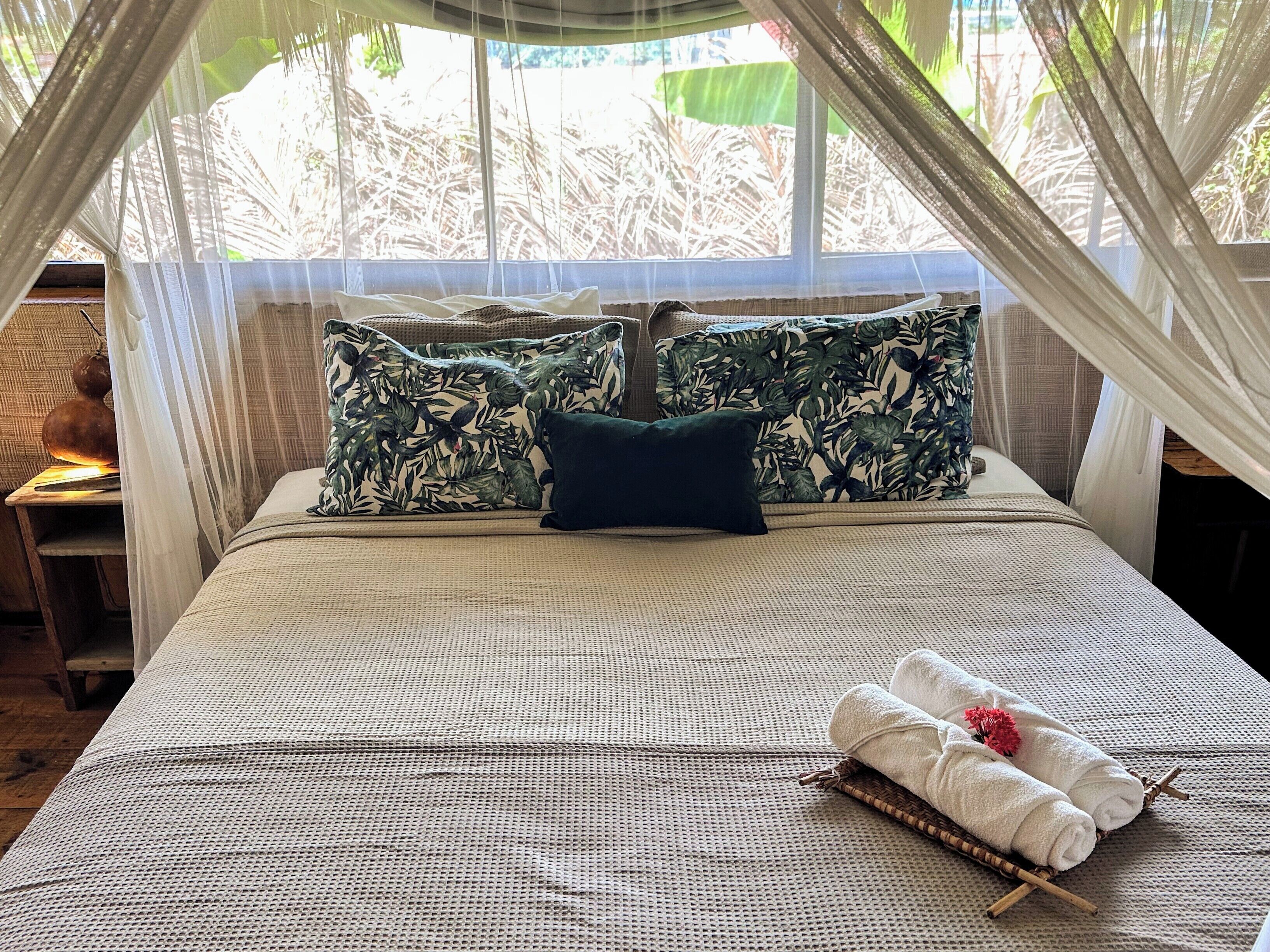 Una cama con dosel, un almohadón y una toalla enrollada con una flor.