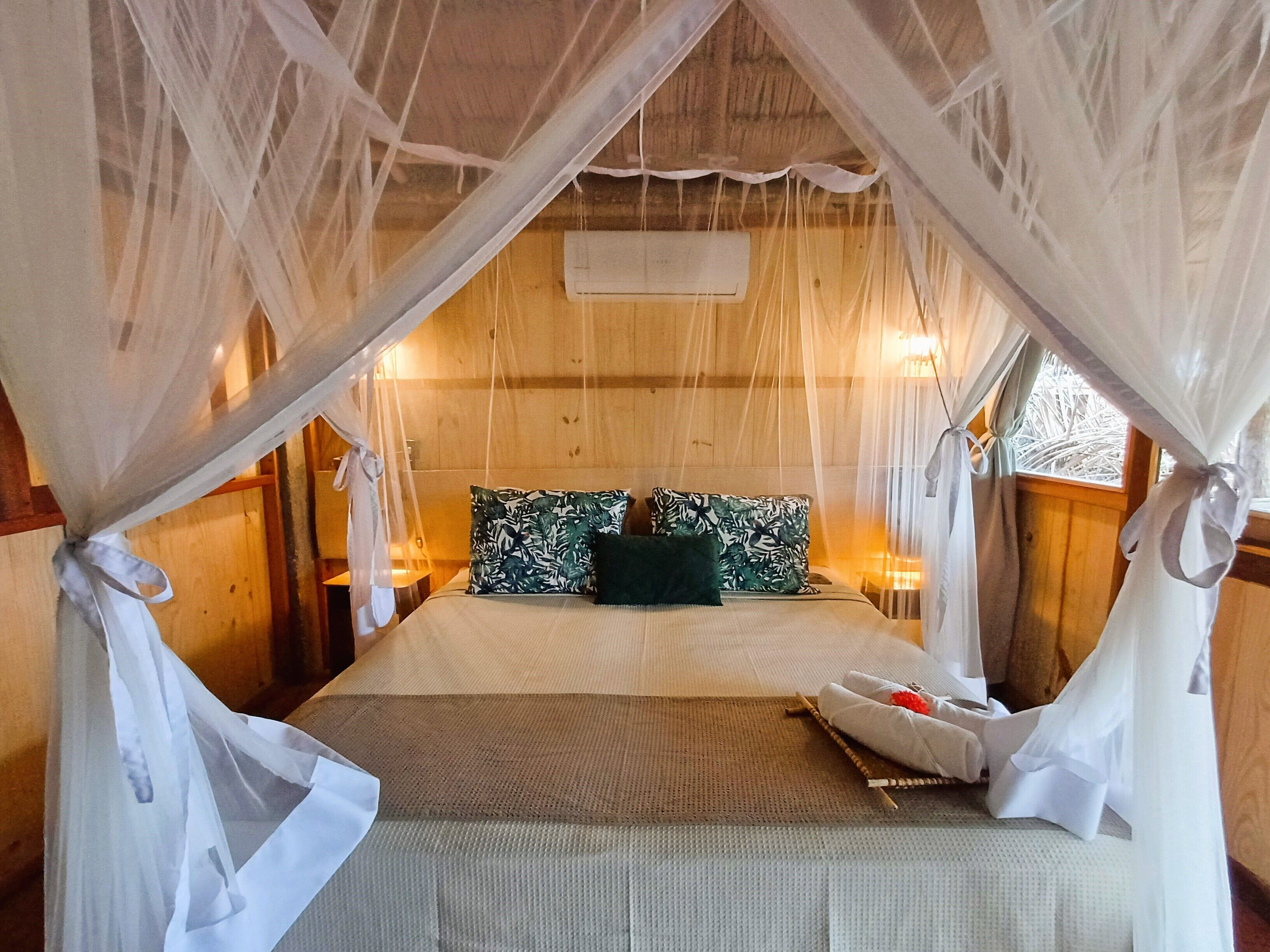 A room with a bed, white curtains, and a wooden ceiling.