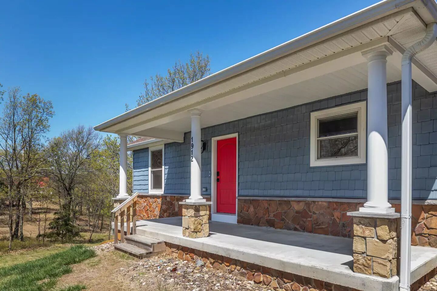 A house with a stone foundation, a red door, and a porch with white columns.