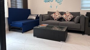 Een woonkamer met een blauwe bank, een grijze bank en een glazen salontafel.