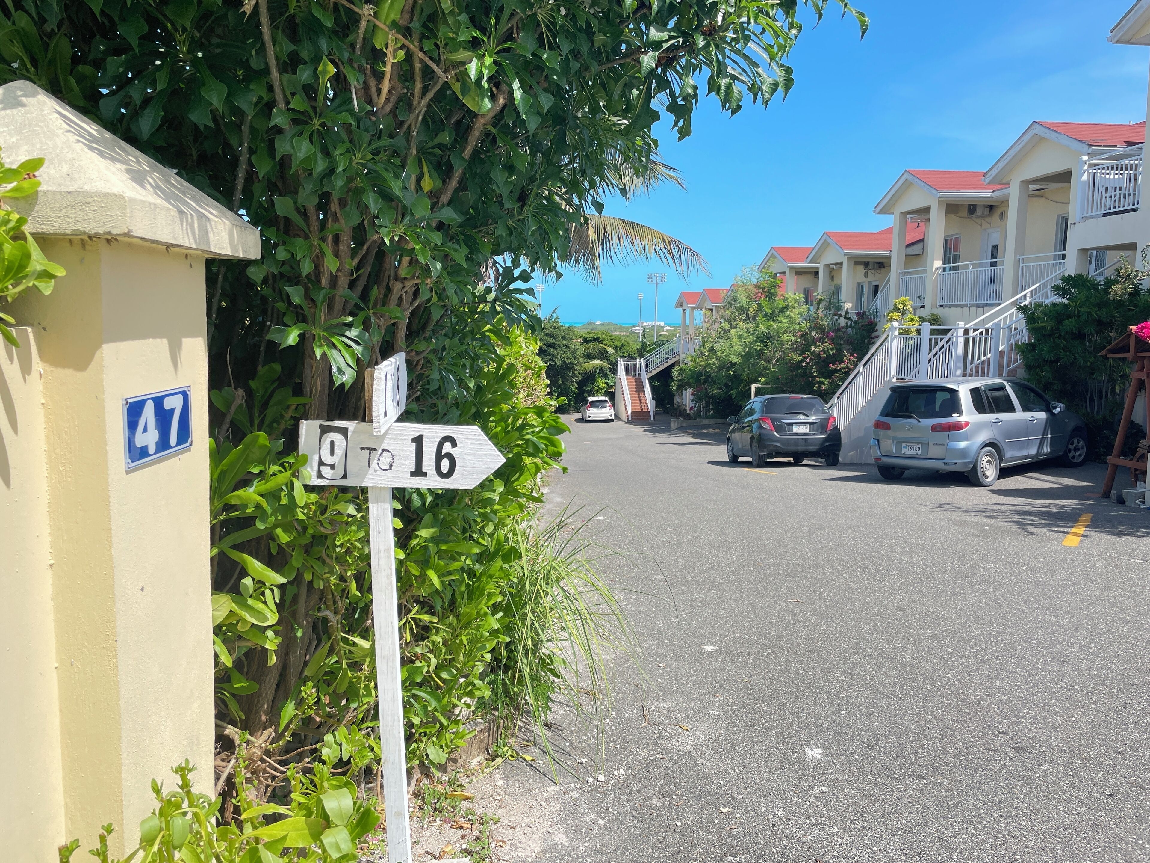A residential street with houses, a street sign, and parked cars.
