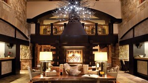 A spacious lobby with a high ceiling, stone walls, and a central chandelier. There are multiple seating areas with lamps and a fireplace. - Boutique Resort in Vail Village -  3 BR - 3BA Residence at The Sebastian (Vail)