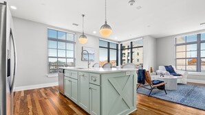 A modern kitchen with a central island, large windows, and a seating area with a blue rug. - Custom Suite over Target - Downtown AU 209 (Auburn)
