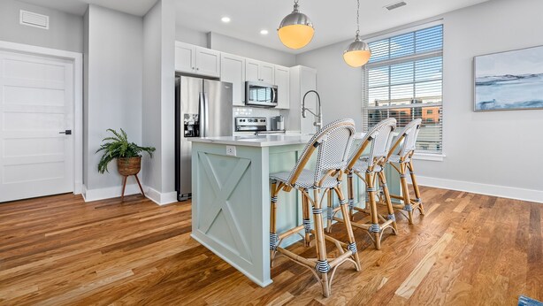 A modern kitchen with white cabinets, stainless steel appliances, and a central island with bar stools. - Custom Suite over Target - Downtown AU 209 (Auburn)