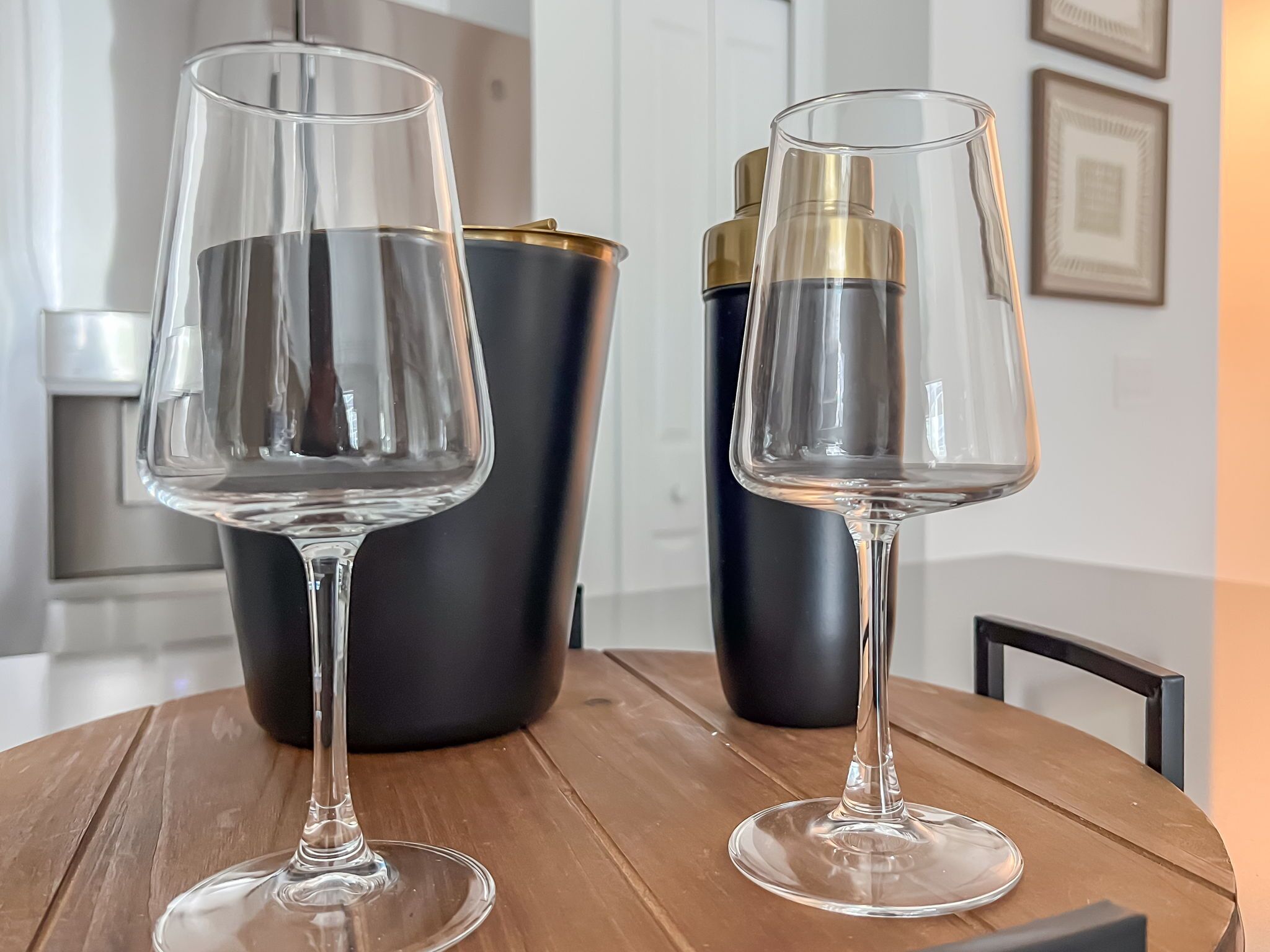 Two wine glasses on a wooden table with a black and gold container in the background.