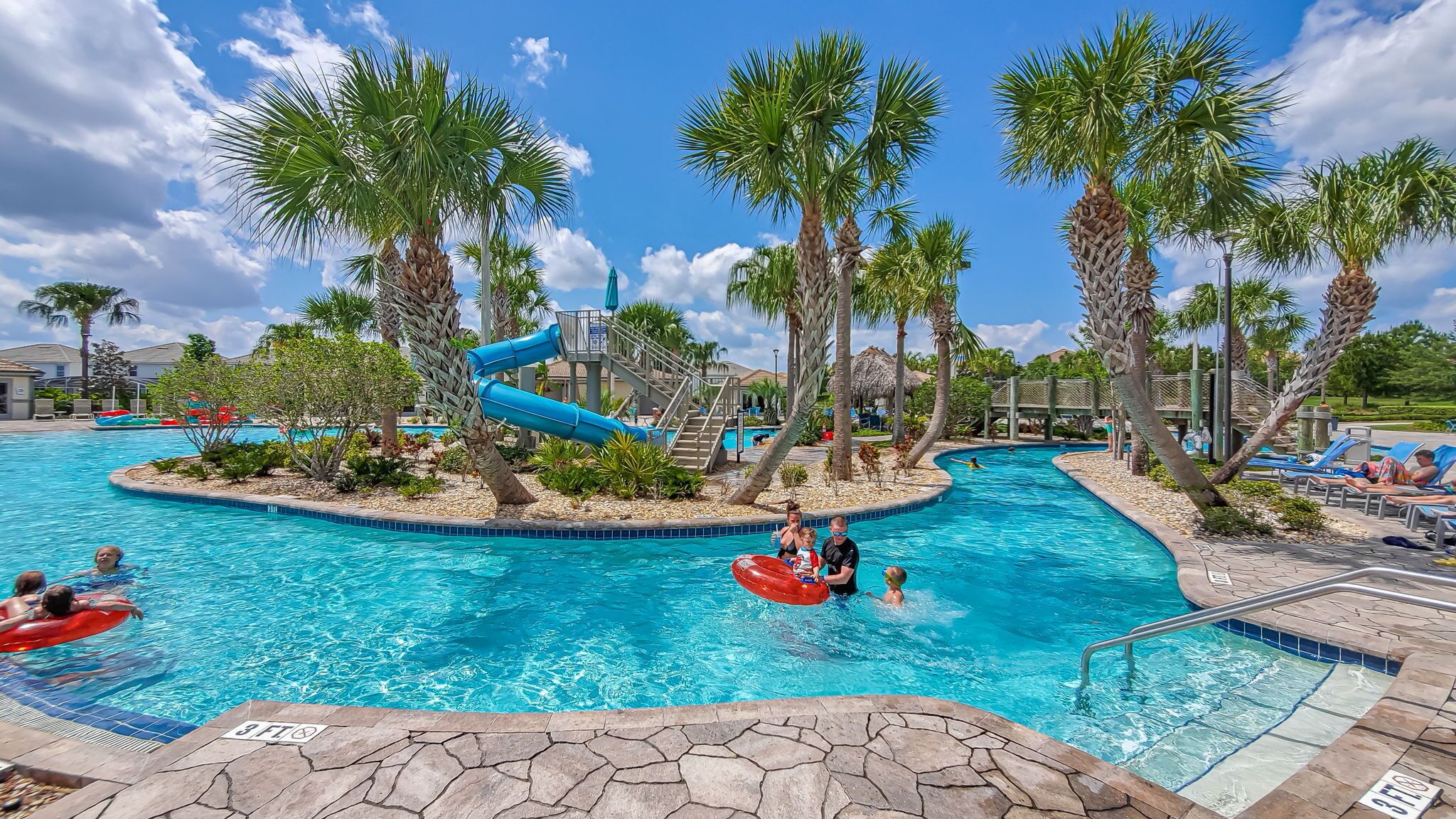A pool area with palm trees, a water slide, and lounge chairs.