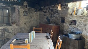 A rustic wooden dining table with chairs, a woven hanging light fixture, and stone walls.