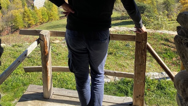 A person standing at a wooden viewing platform with a mountainous landscape in the background.