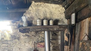 A rustic kitchen with a wood-burning stove, metal containers, and a hanging grater.