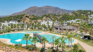 A resort with a large swimming pool, multiple lounge areas, and a mountainous backdrop.