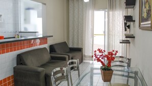 A modern kitchen with a tiled backsplash, a dining area with a glass table, and a sofa. - Residencial Blaia  (Praia Grande)