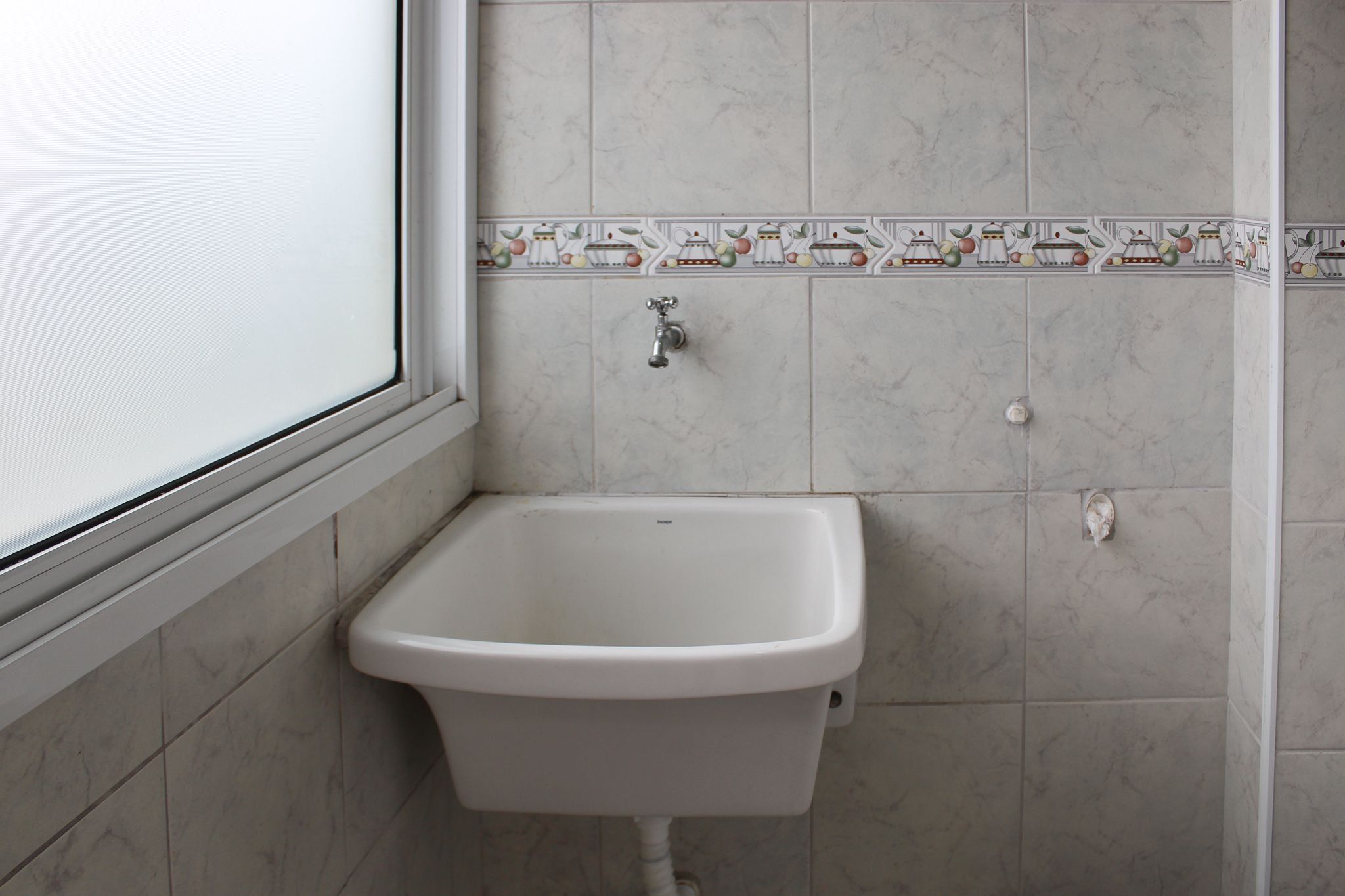 Een badkamer met een witte wastafel met voetstuk, een wandmengkraan en een decoratieve tegelrand.