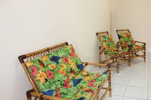 A room with a seating area featuring wicker chairs with colorful floral upholstery. - Residencial Blaia  (Praia Grande)
