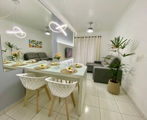 Uma sala de estar moderna com área de jantar, um sofá cinza, um espelho grande e um vaso com planta.