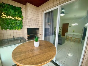 A kitchen with a built-in oven, a round wooden table, and a green wall decoration. - Residencial Blaia  (Praia Grande)