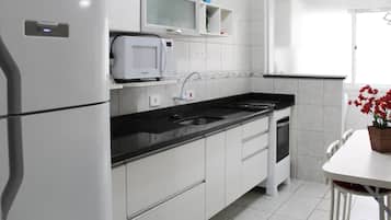 Una cocina moderna con armarios blancos, microondas integrado, un lavamanos y un comedor con mesa y sillas.