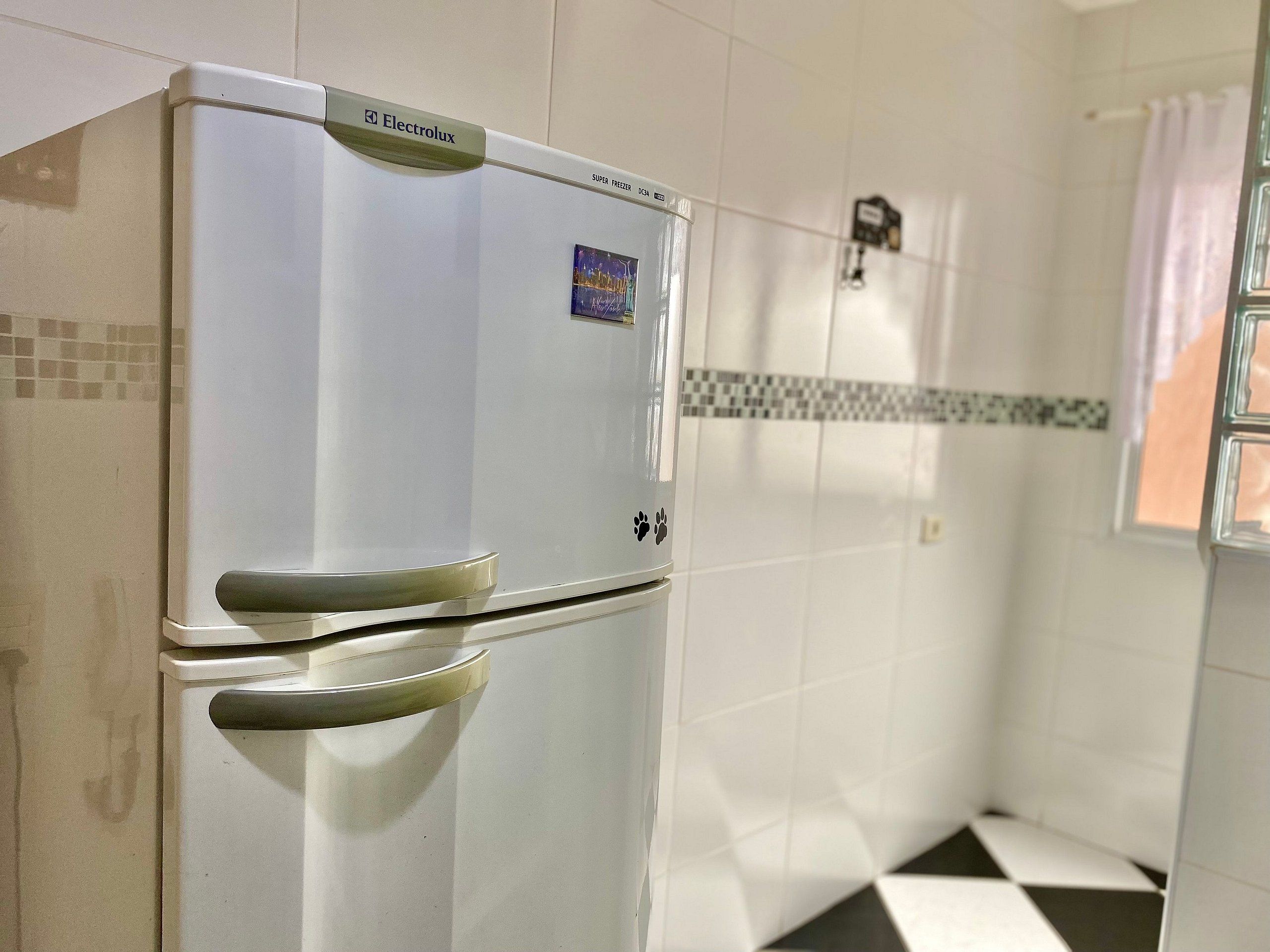 A white Electrolux refrigerator in a kitchen with tiled walls and a checkered floor.